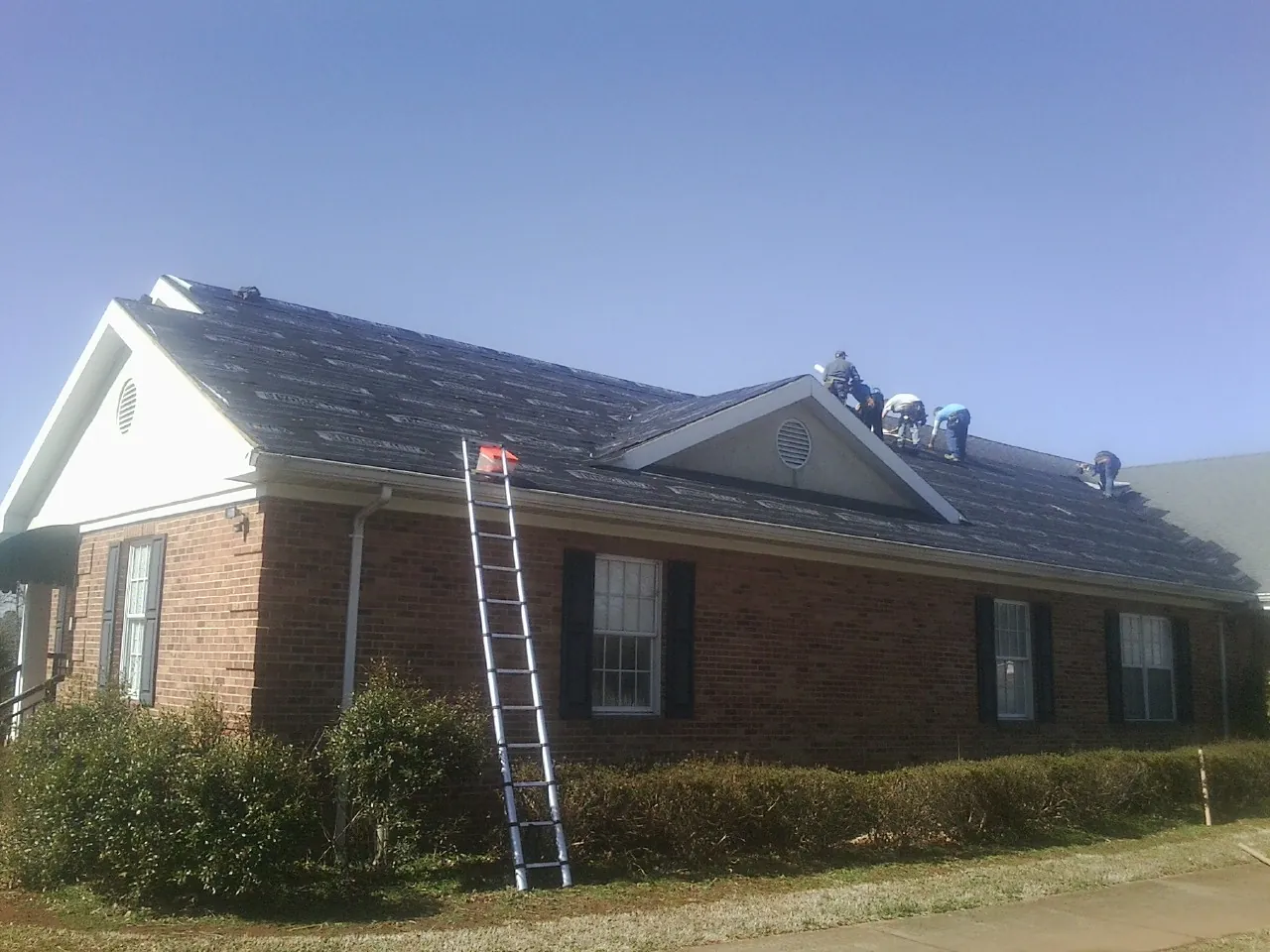 Crew tearing shingles off a brick ranch roof with a ladder set — Emergency Roof Repair work by our crew in Lynnville
