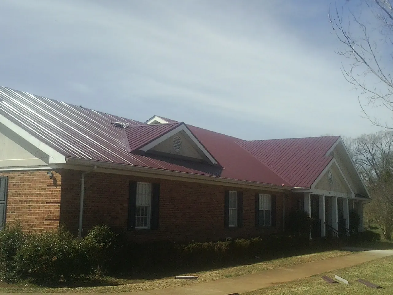 Red metal roof with gabled entries on a long brick building, from a Hail Damage Roof Repair job in Lynnville