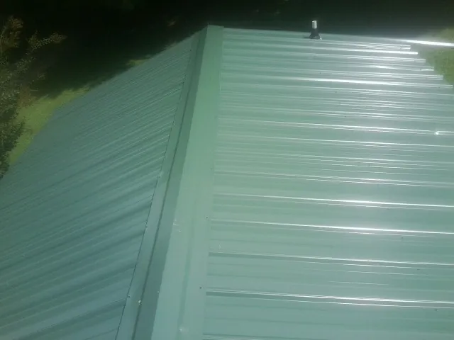 New green metal panels meeting at the ridge of a roof — Flat Roof Repair work by our crew in Lynnville