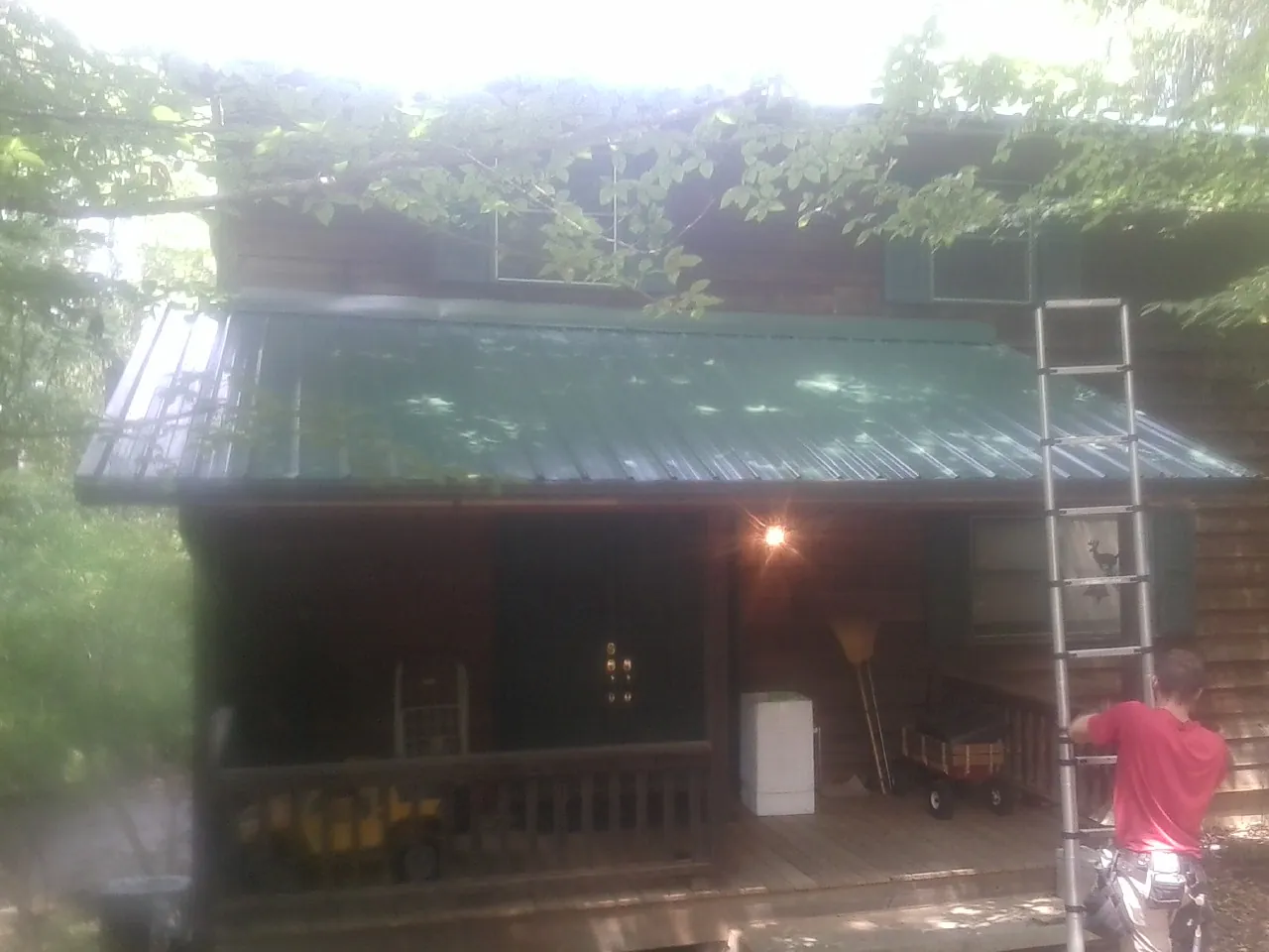 Worker on a ladder at the green porch roof of a wooded cabin in Lynnville
