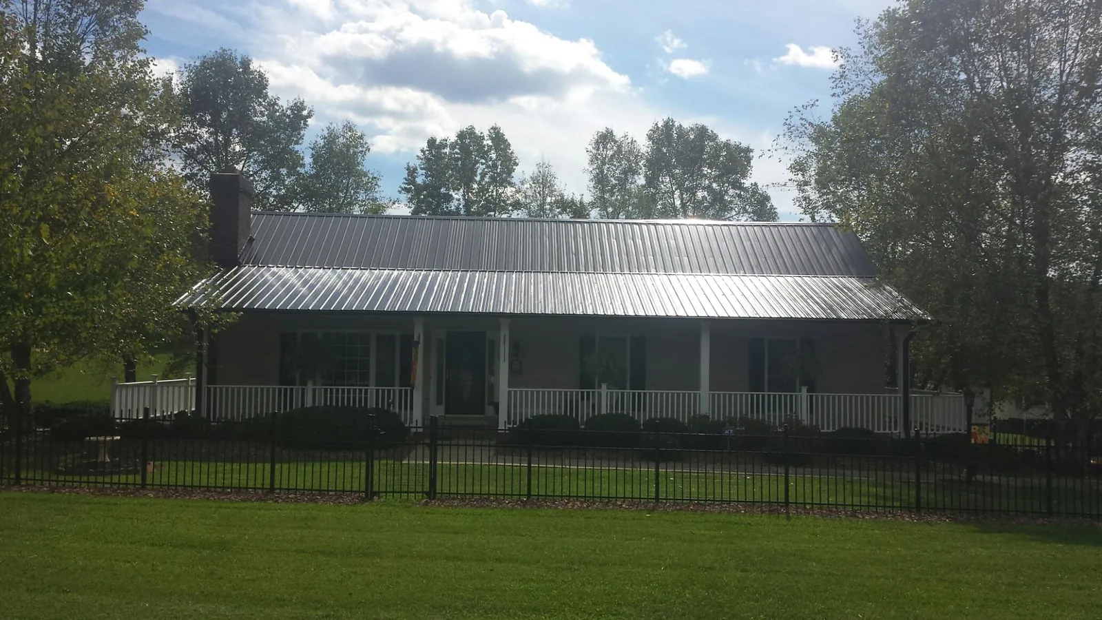 Gray metal roof on a brick ranch with a full width front porch — Gutter Guard Installation work by our crew in Lynnville