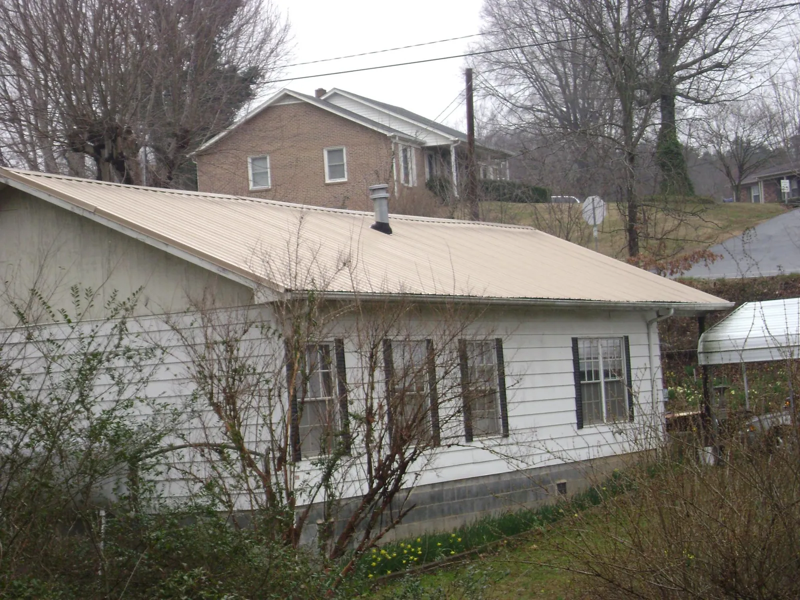 Tan metal roof on a white sided house set into a hillside — Commercial Roofing by Roofing Brothers in Lynnville